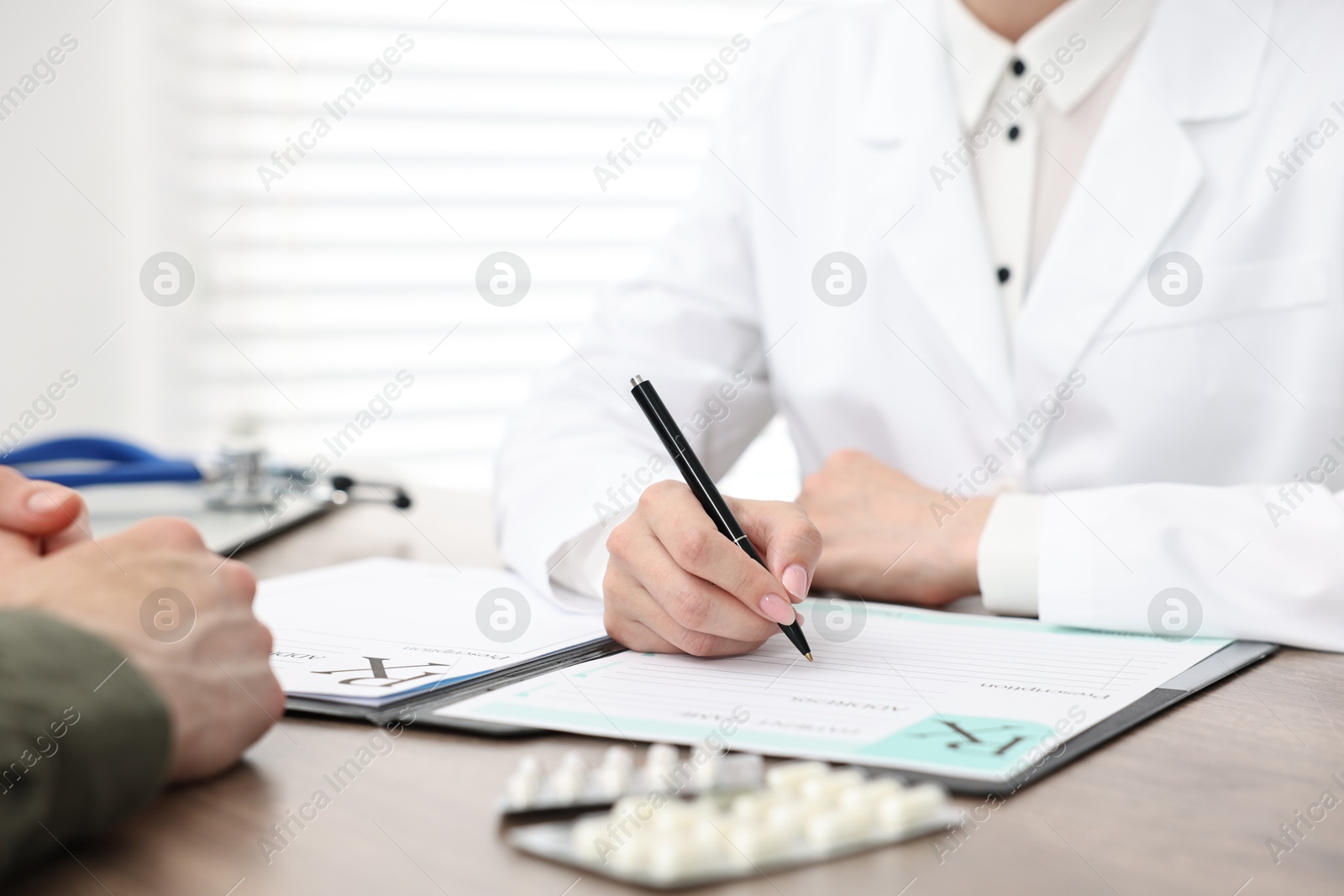 Photo of Doctor writing prescription for patient at wooden table in clinic, closeup