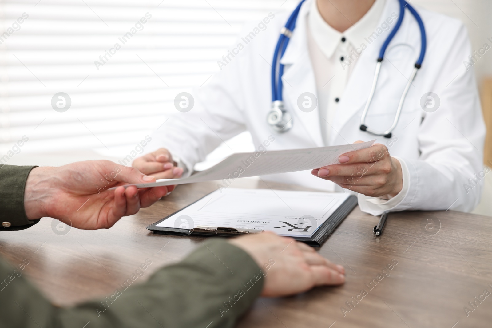 Photo of Doctor giving prescription to patient at wooden table in clinic, closeup