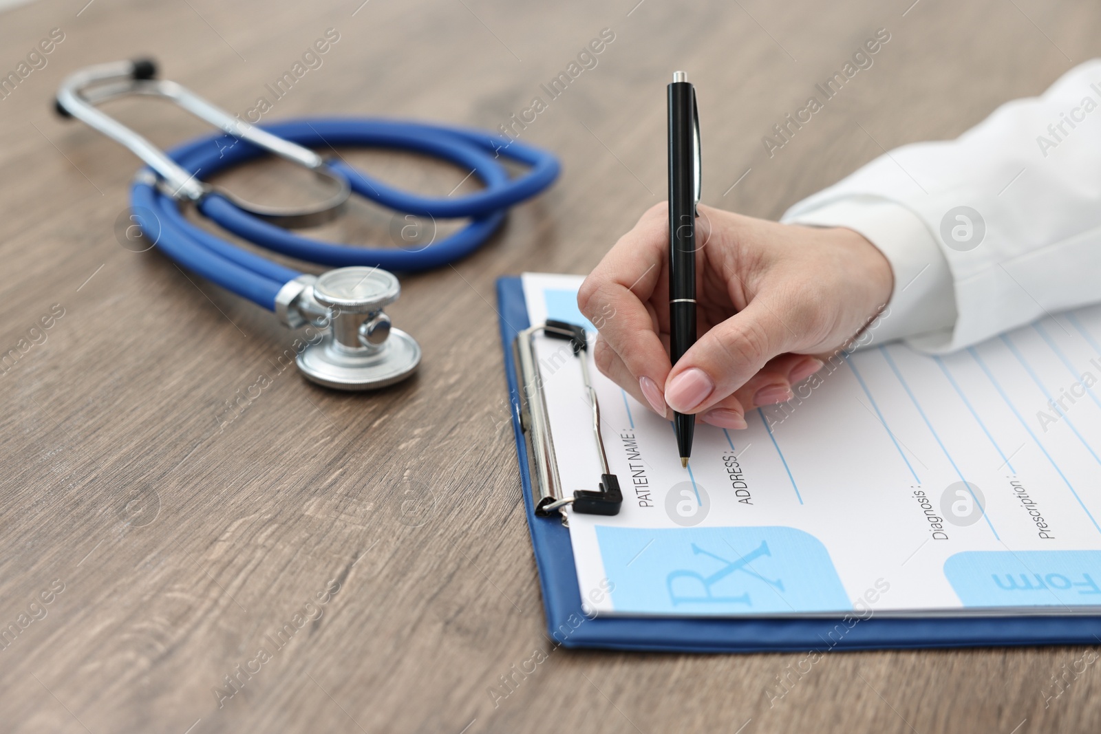 Photo of Doctor writing prescription at wooden table in clinic, closeup