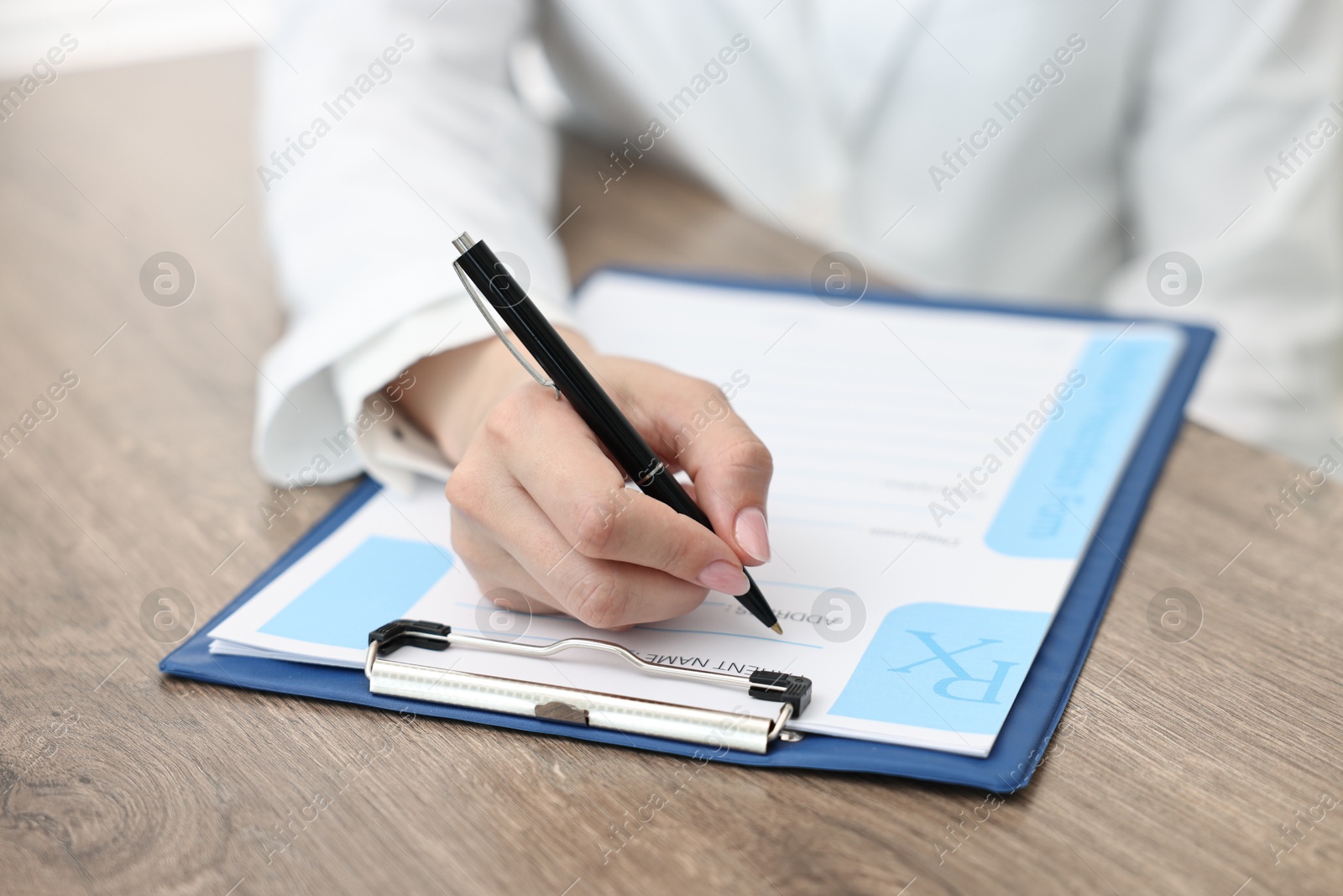 Photo of Doctor writing prescription at wooden table in clinic, closeup