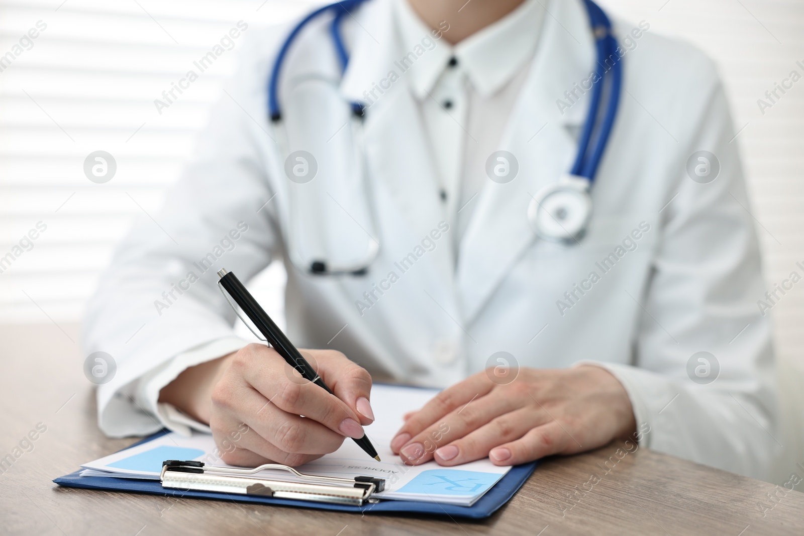 Photo of Doctor writing prescription at wooden table in clinic, closeup