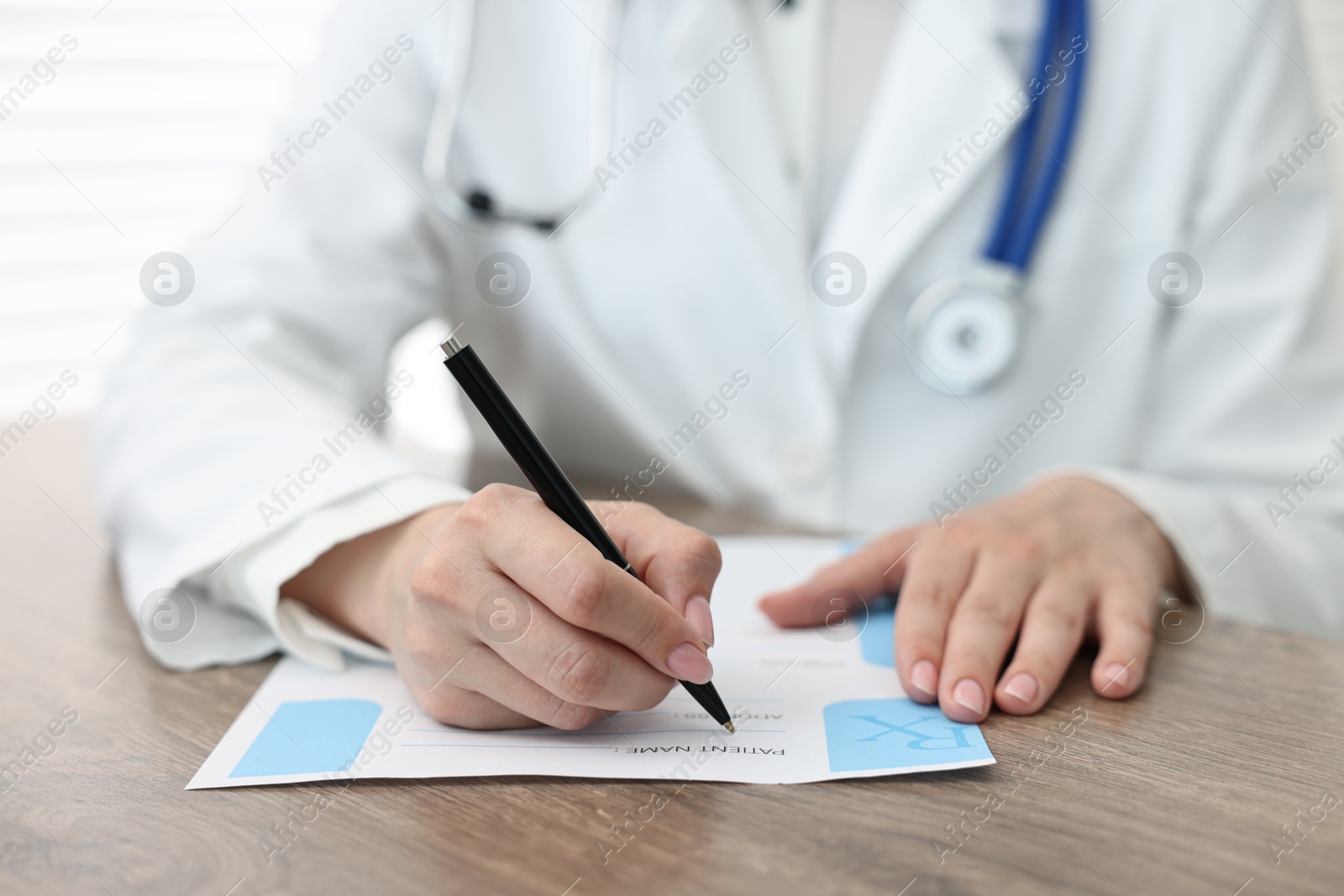 Photo of Doctor writing prescription at wooden table in clinic, closeup