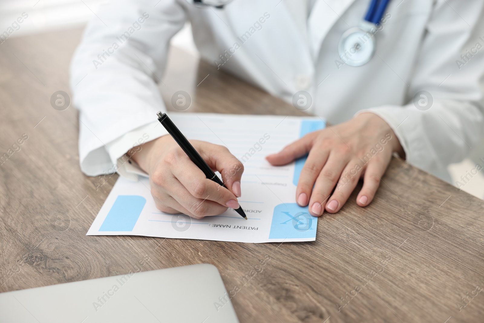 Photo of Doctor writing prescription at wooden table in clinic, closeup