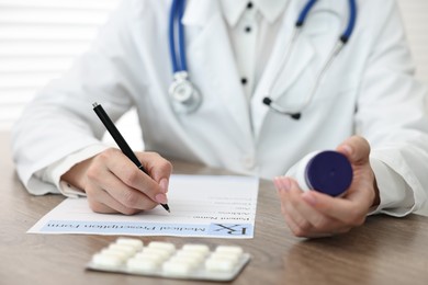 Photo of Doctor with pills writing prescription at wooden table in clinic, closeup