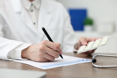 Photo of Doctor with pills writing prescription at wooden table in clinic, closeup