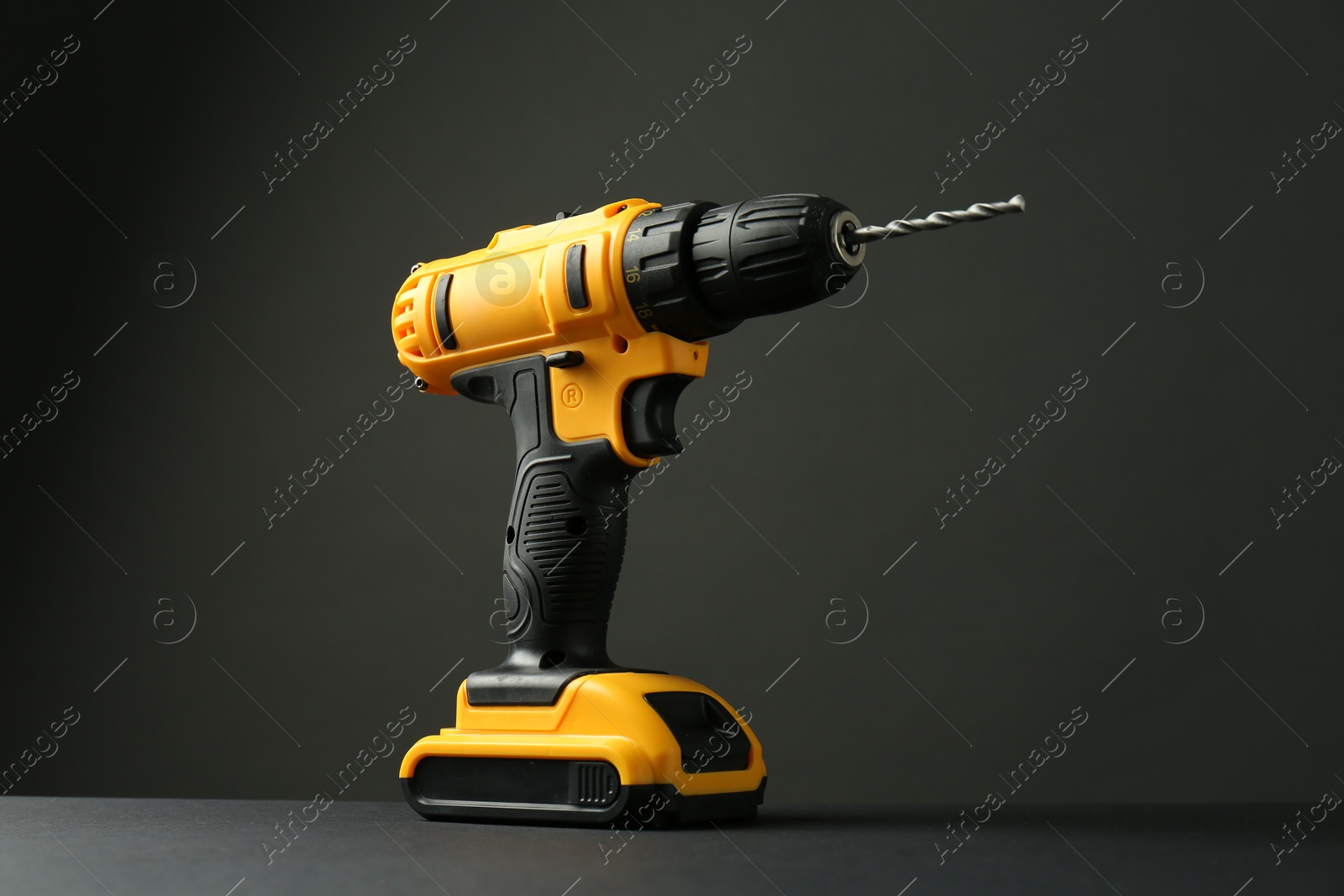 Photo of Modern cordless electric drill on grey table against black background