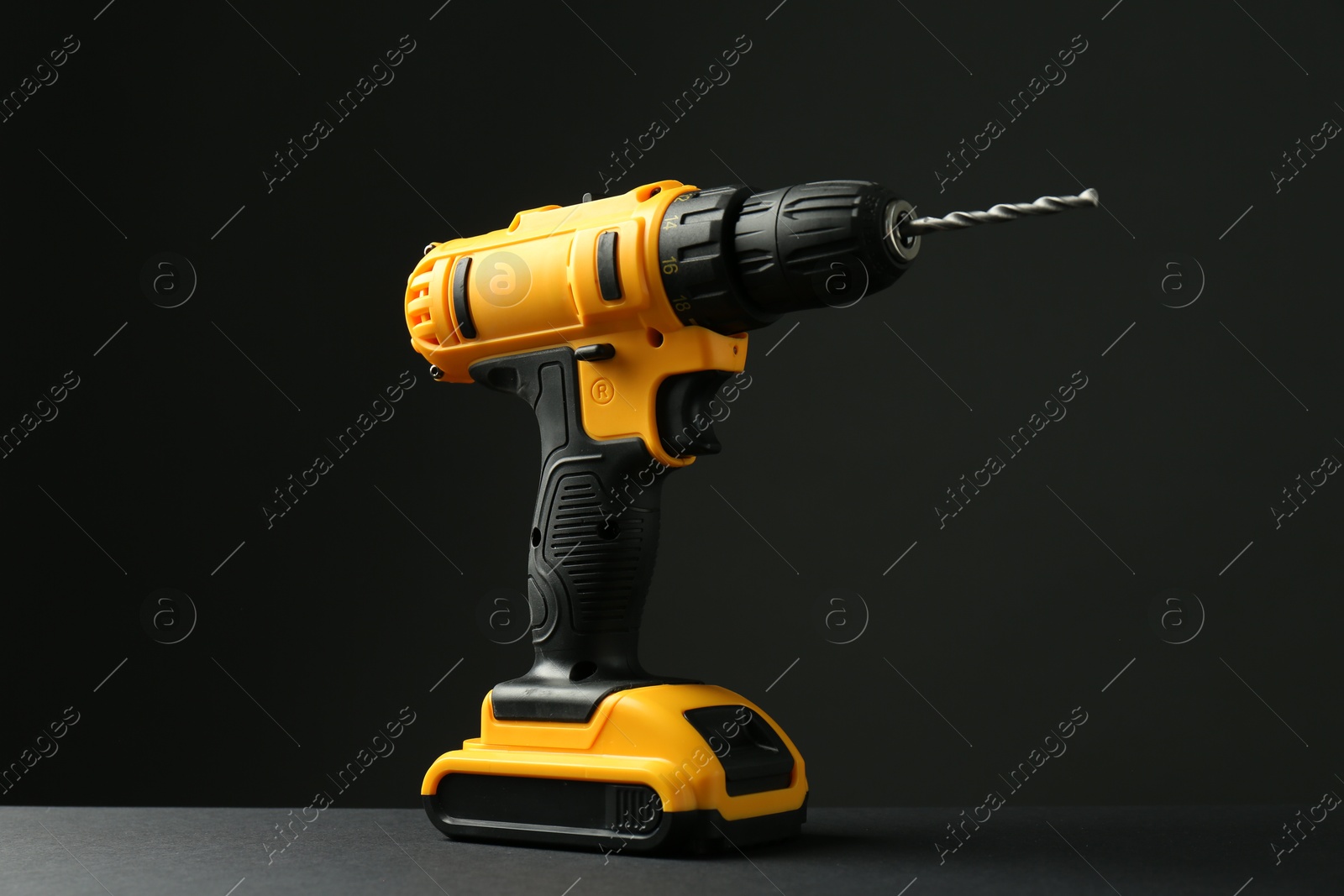 Photo of Modern cordless electric drill on grey table against black background