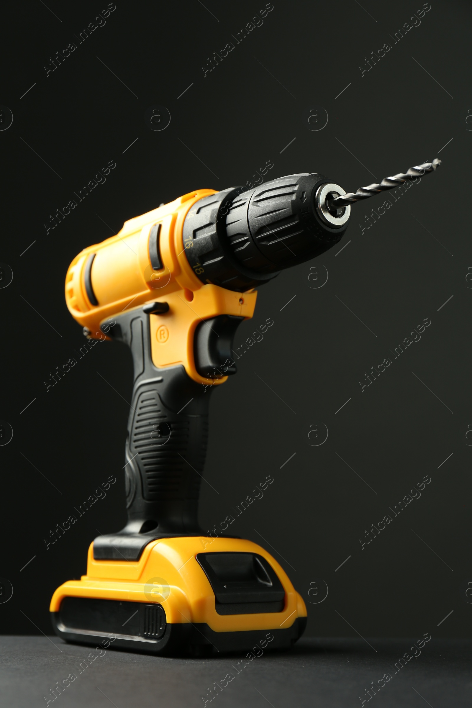 Photo of Modern cordless electric drill on grey table against black background