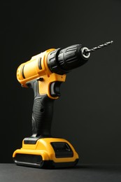 Photo of Modern cordless electric drill on grey table against black background