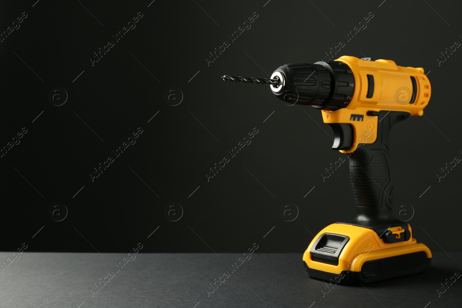 Photo of Modern cordless electric drill on grey table against black background. Space for text