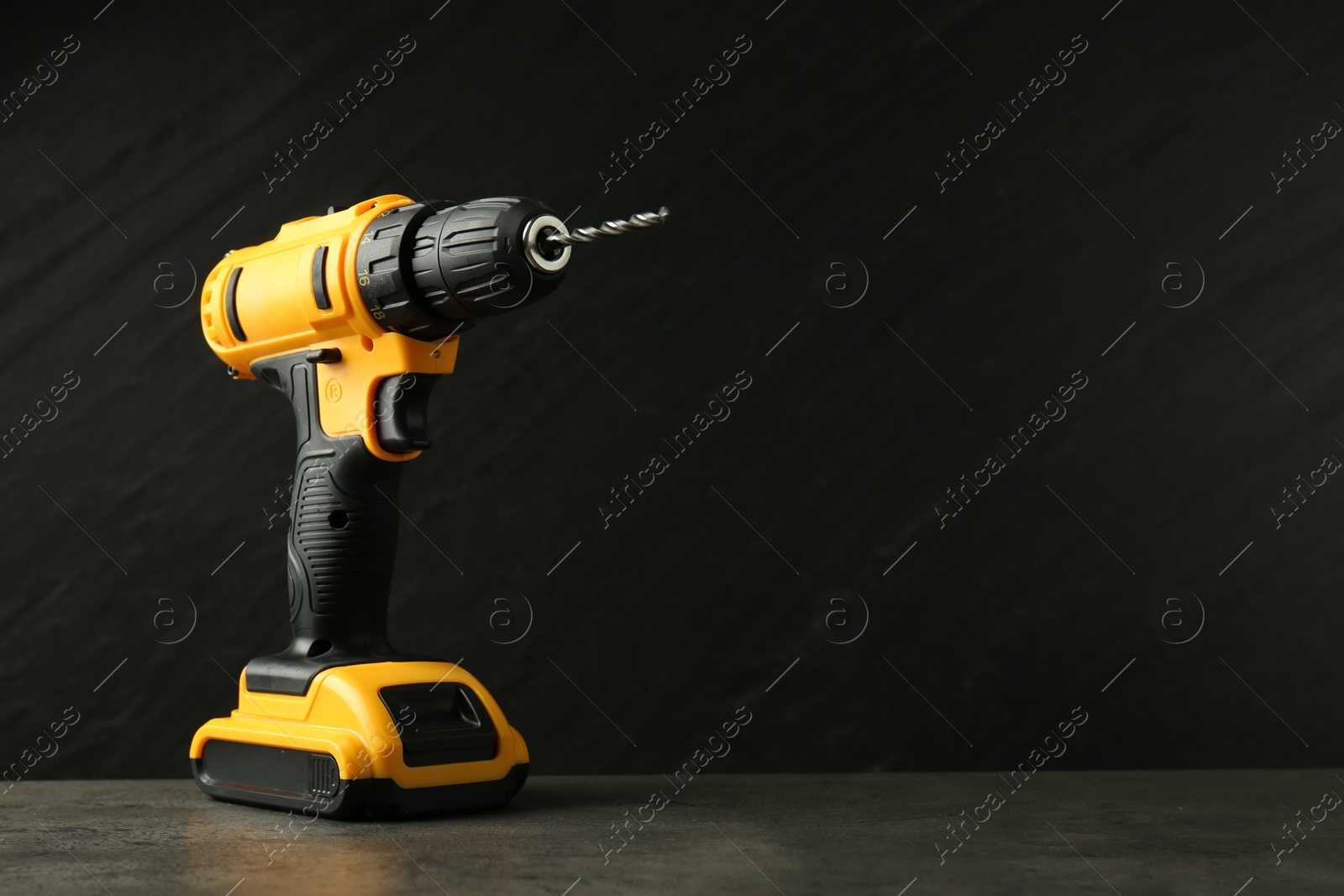 Photo of Modern cordless electric drill on grey table against black background. Space for text