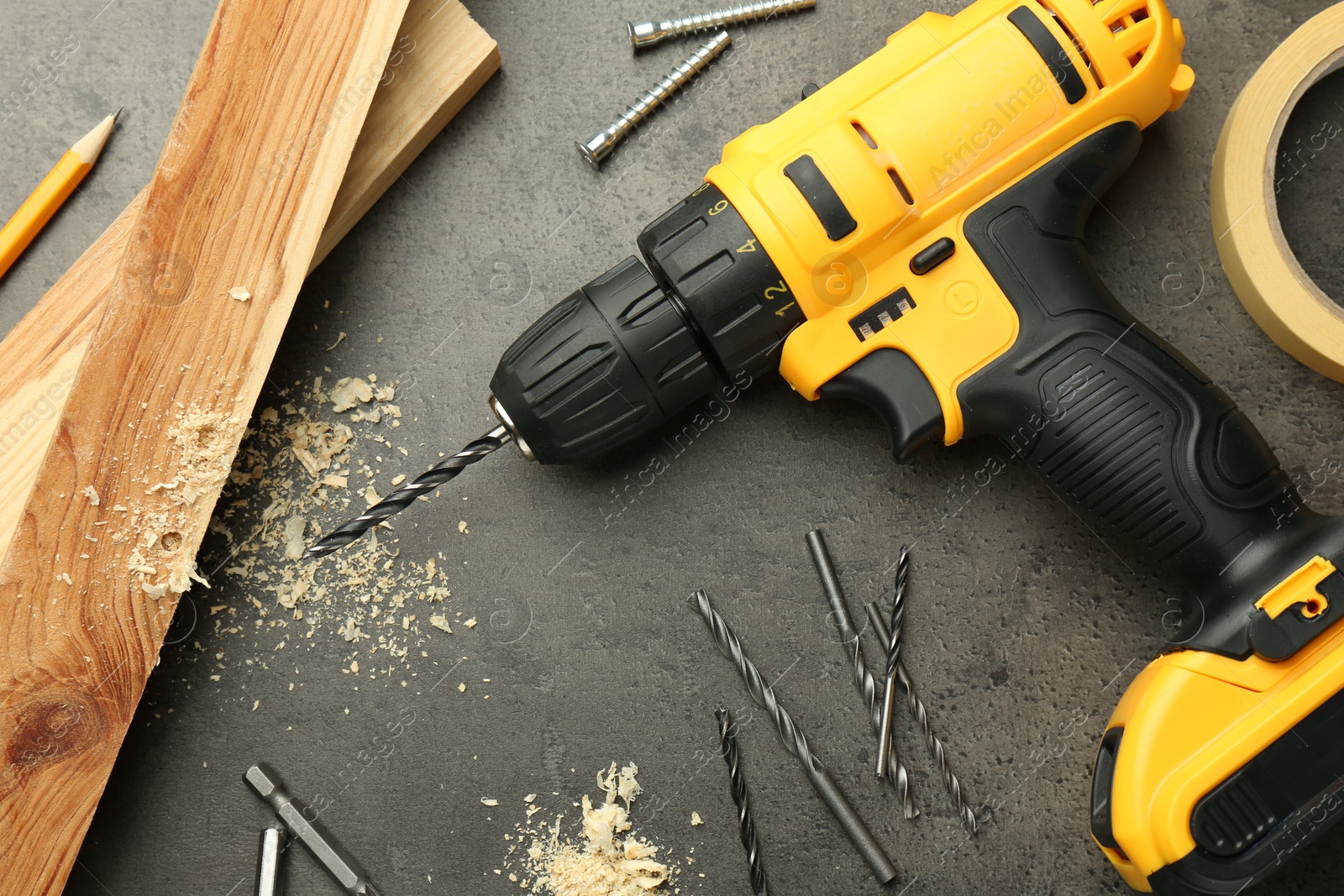 Photo of Modern cordless electric drill, sawdust, planks and bits on grey table, flat lay