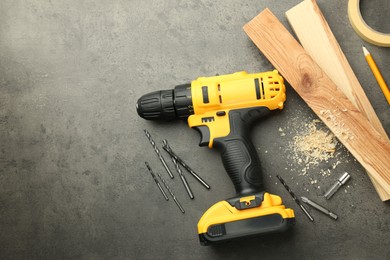 Modern cordless electric drill, sawdust, planks and bits on grey table, flat lay