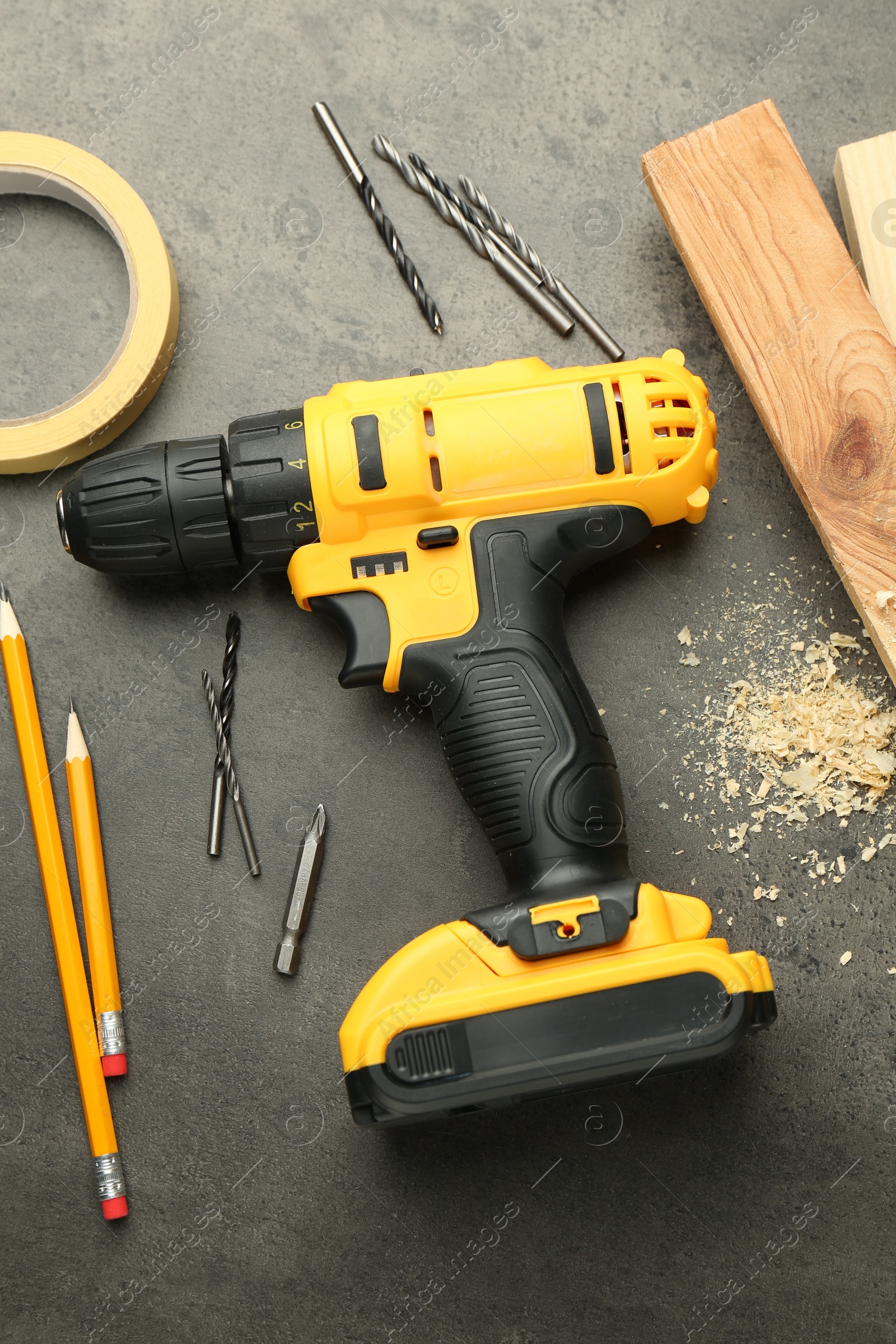 Photo of Modern cordless electric drill, sawdust, planks and bits on grey table, flat lay