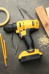 Modern cordless electric drill, sawdust, planks and bits on grey table, flat lay