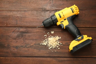 Photo of Modern cordless electric drill and sawdust on wooden table, top view. Space for text