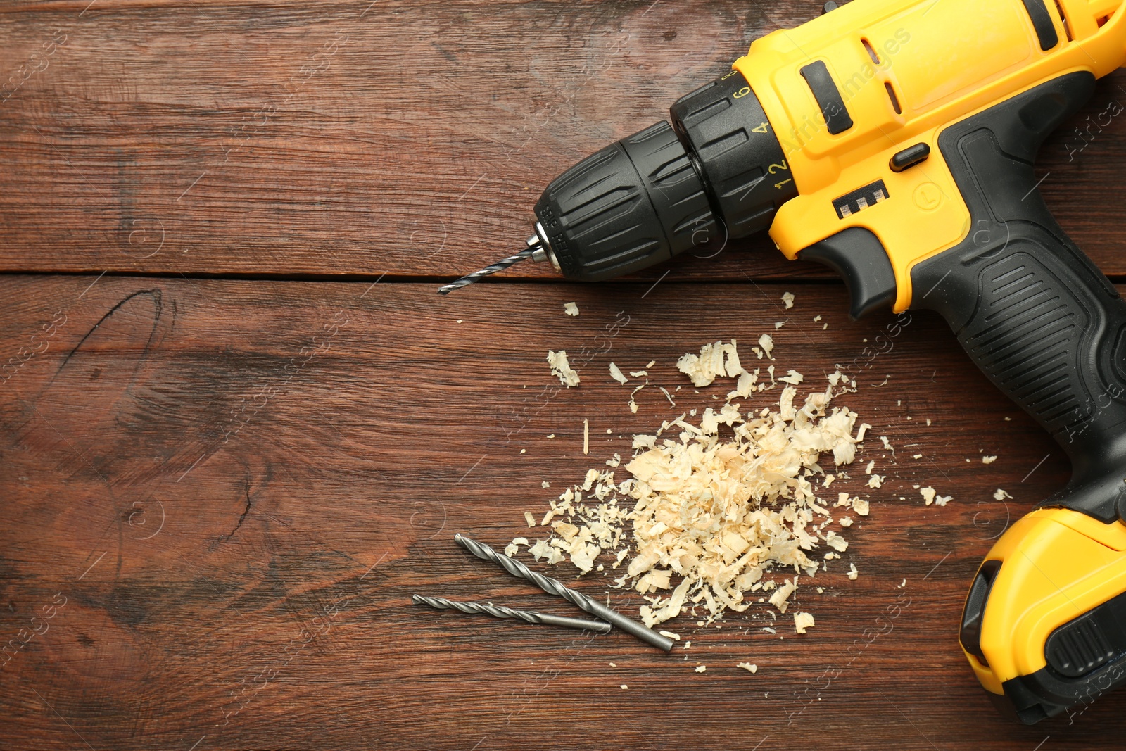 Photo of Modern cordless electric drill, sawdust and bits on wooden table, top view. Space for text