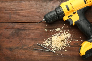 Modern cordless electric drill, sawdust and bits on wooden table, top view. Space for text