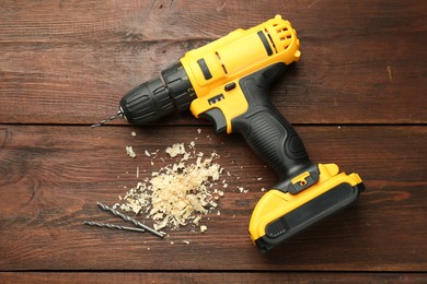 Modern cordless electric drill, sawdust and bits on wooden table, top view