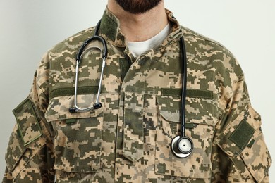 Photo of Man in military uniform with stethoscope on light background, closeup. Health care concept