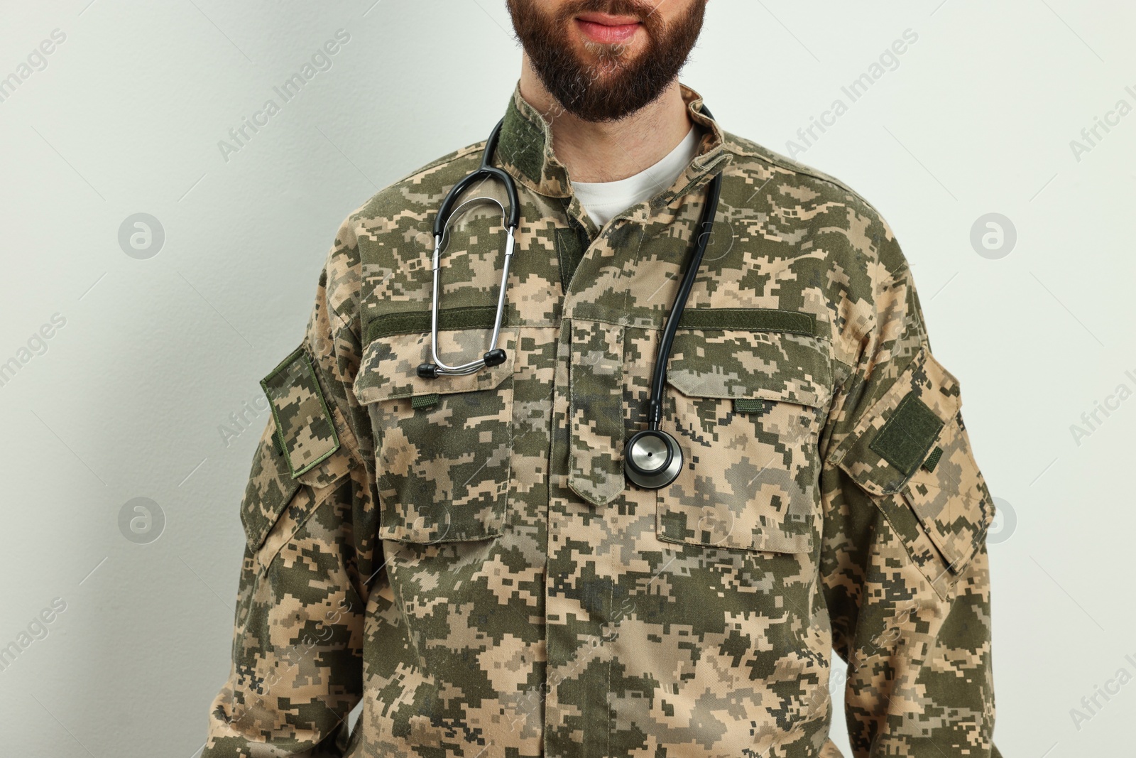 Photo of Man in military uniform with stethoscope on light background, closeup. Health care concept