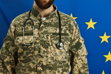 Photo of Man in military uniform with stethoscope against flag of European Union, closeup. Health care concept