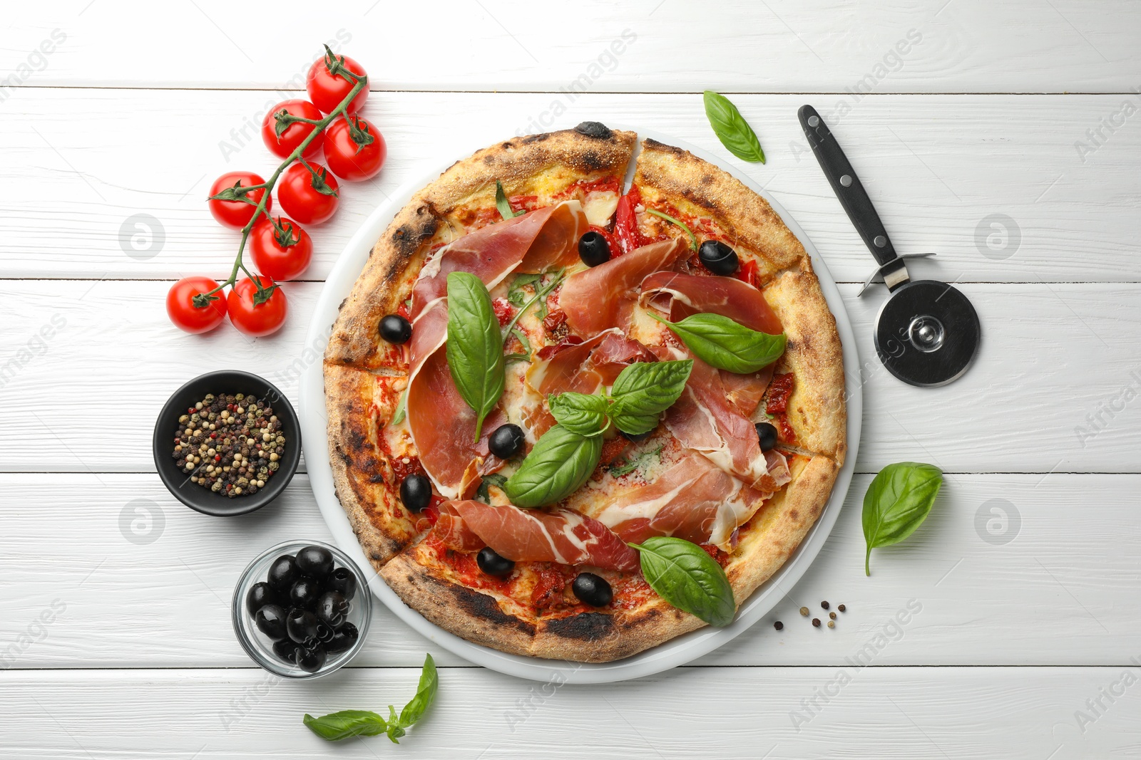 Photo of Tasty pizza with cured ham, olives, tomatoes and basil on white wooden table, flat lay