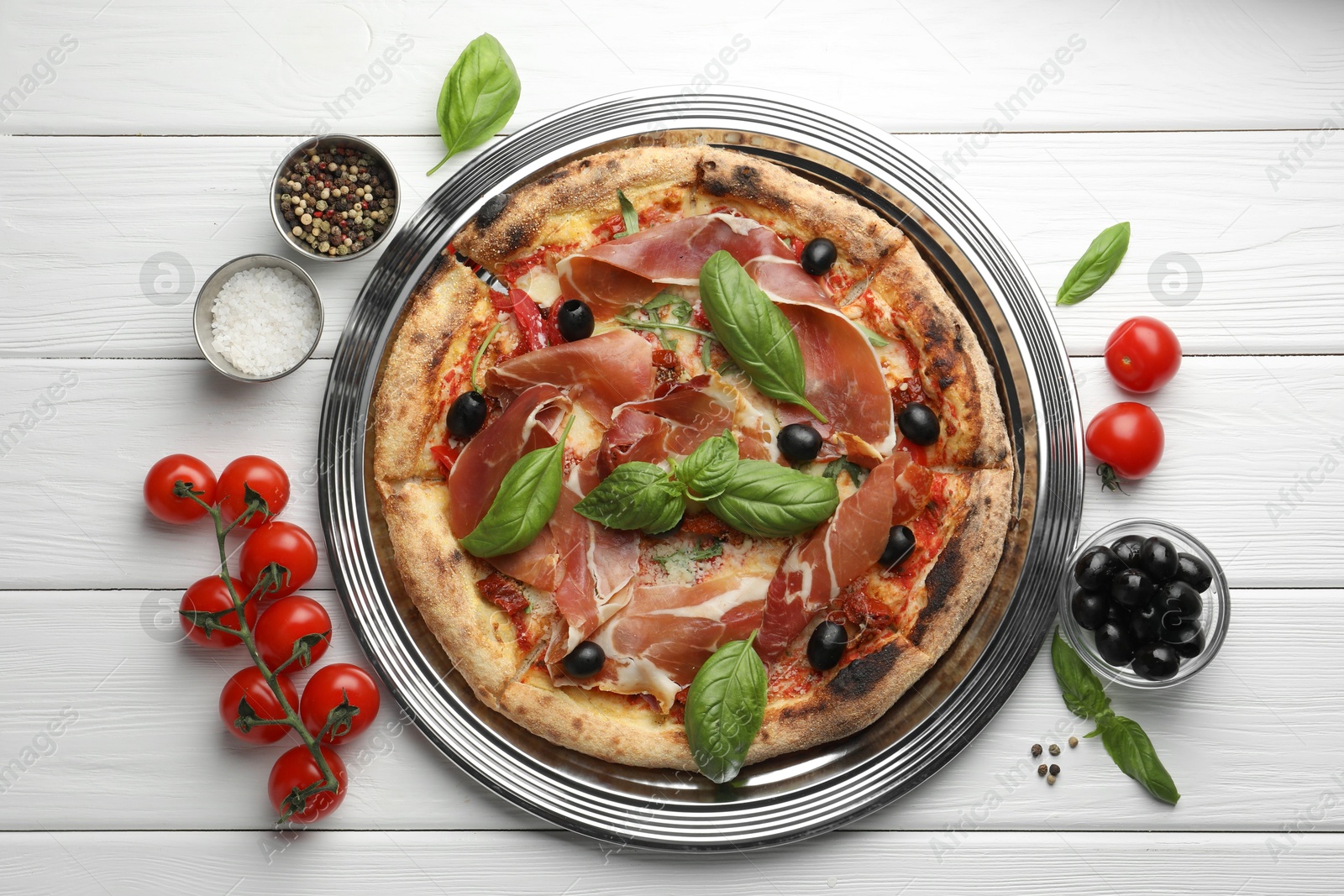 Photo of Tasty pizza with cured ham, olives, tomatoes and basil on white wooden table, flat lay