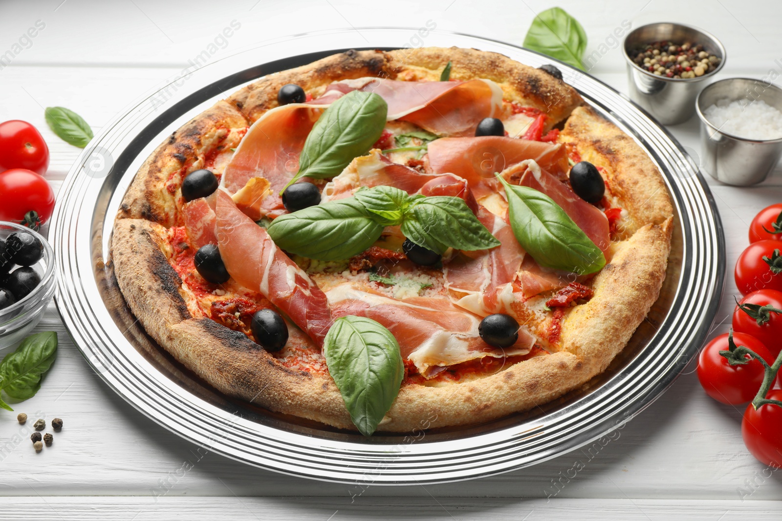 Photo of Tasty pizza with cured ham, olives, tomatoes and basil on white wooden table, closeup