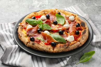 Photo of Tasty pizza with cured ham, olives, mozzarella cheese, sun-dried tomato and basil on gray table, closeup