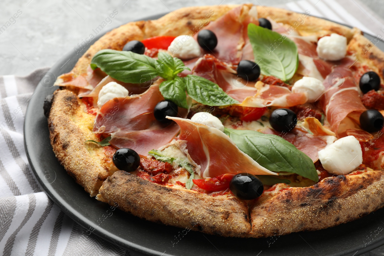 Photo of Tasty pizza with cured ham, olives, mozzarella cheese, sun-dried tomato and basil on table, closeup