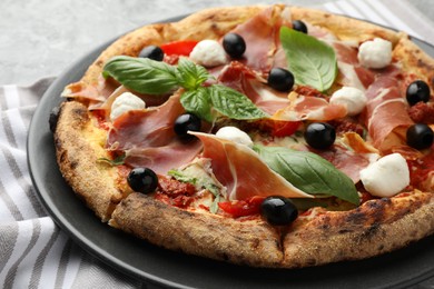 Tasty pizza with cured ham, olives, mozzarella cheese, sun-dried tomato and basil on table, closeup