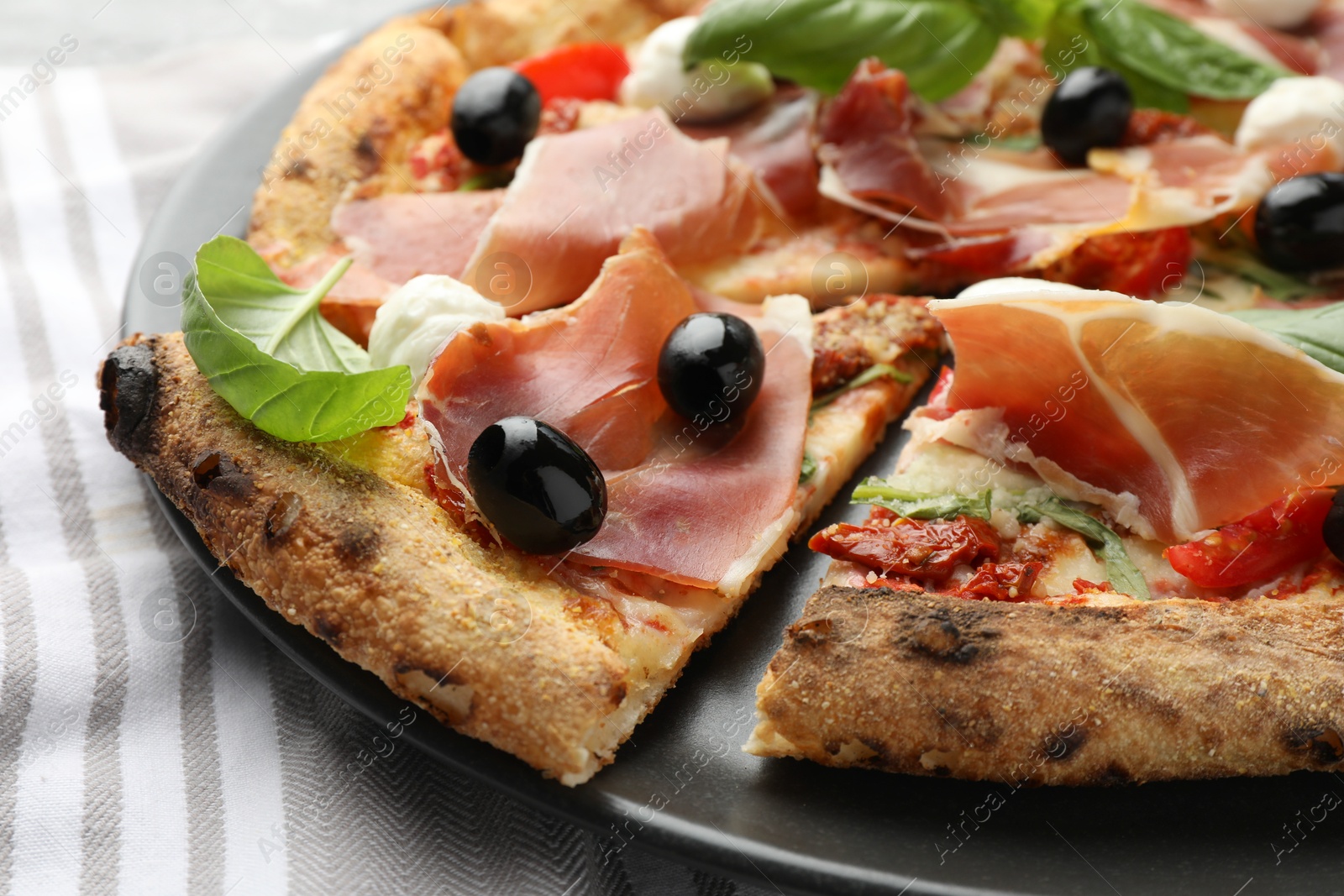 Photo of Tasty pizza with cured ham, olives, mozzarella cheese, sun-dried tomato and basil on table, closeup