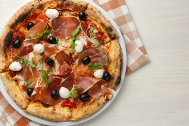 Tasty pizza with cured ham, olives, mozzarella cheese, sun-dried tomato and arugula on light wooden table, top view. Space for text