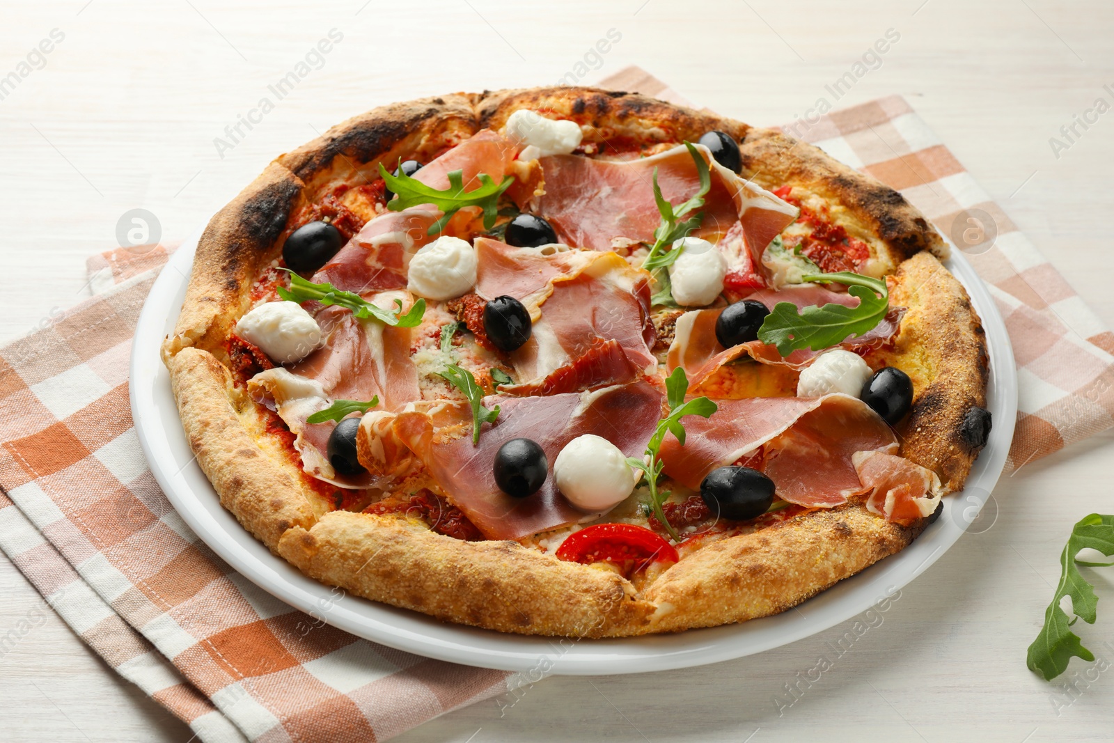 Photo of Tasty pizza with cured ham, olives, mozzarella cheese, sun-dried tomato and arugula on light wooden table