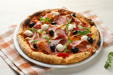 Tasty pizza with cured ham, olives, mozzarella cheese, sun-dried tomato and arugula on light wooden table