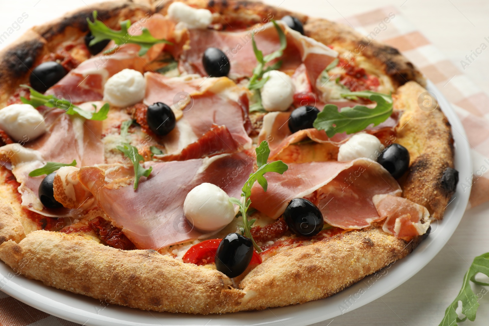 Photo of Tasty pizza with cured ham, olives, mozzarella cheese, sun-dried tomato and arugula on table, closeup