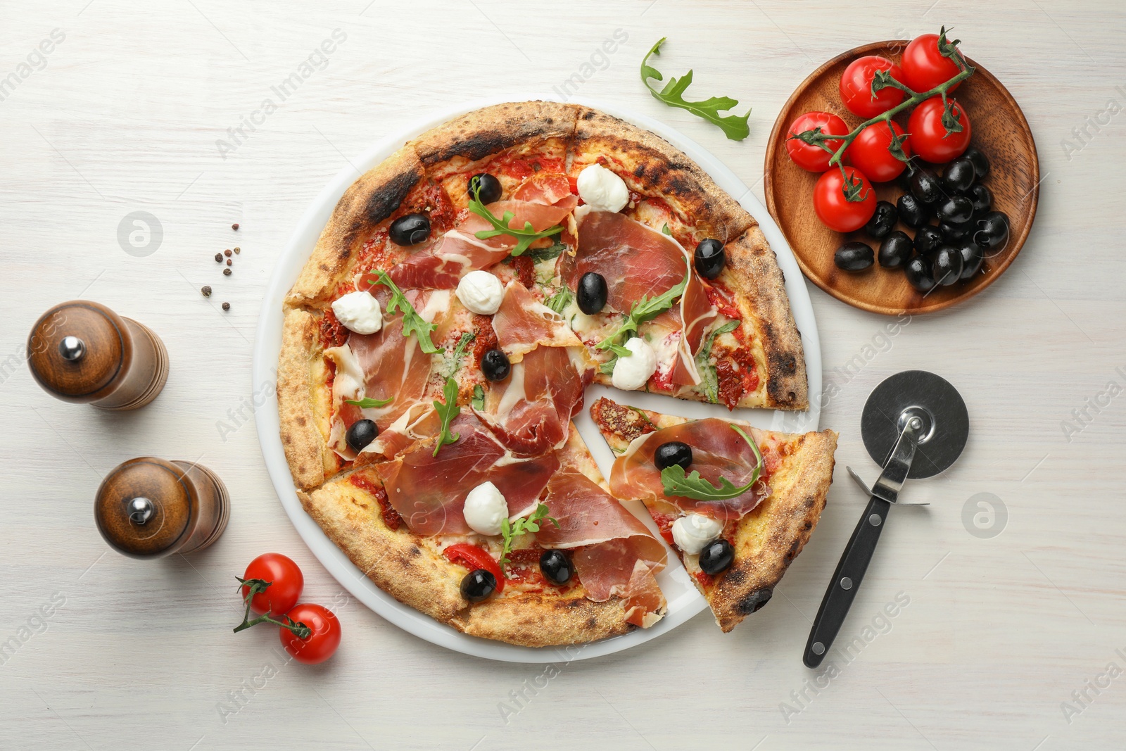 Photo of Tasty pizza with cured ham, olives, mozzarella cheese, tomatoes and arugula on light wooden table, flat lay