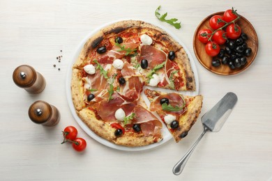 Photo of Tasty pizza with cured ham, olives, mozzarella cheese, tomatoes and arugula on light wooden table, flat lay