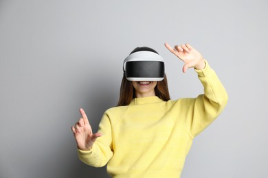 Photo of Smiling woman using virtual reality headset on light grey background