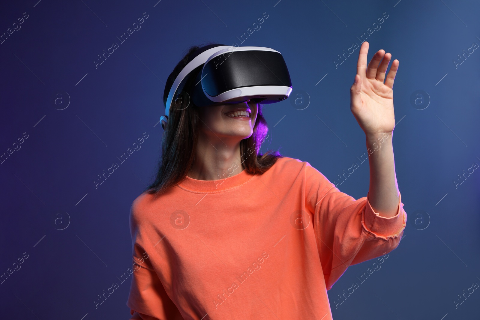 Photo of Smiling woman using virtual reality headset on dark blue background