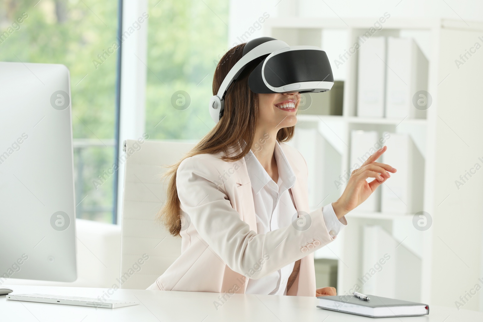 Photo of Smiling woman using virtual reality headset at workplace in office