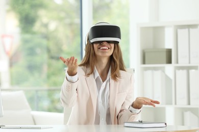 Photo of Smiling woman using virtual reality headset at workplace in office