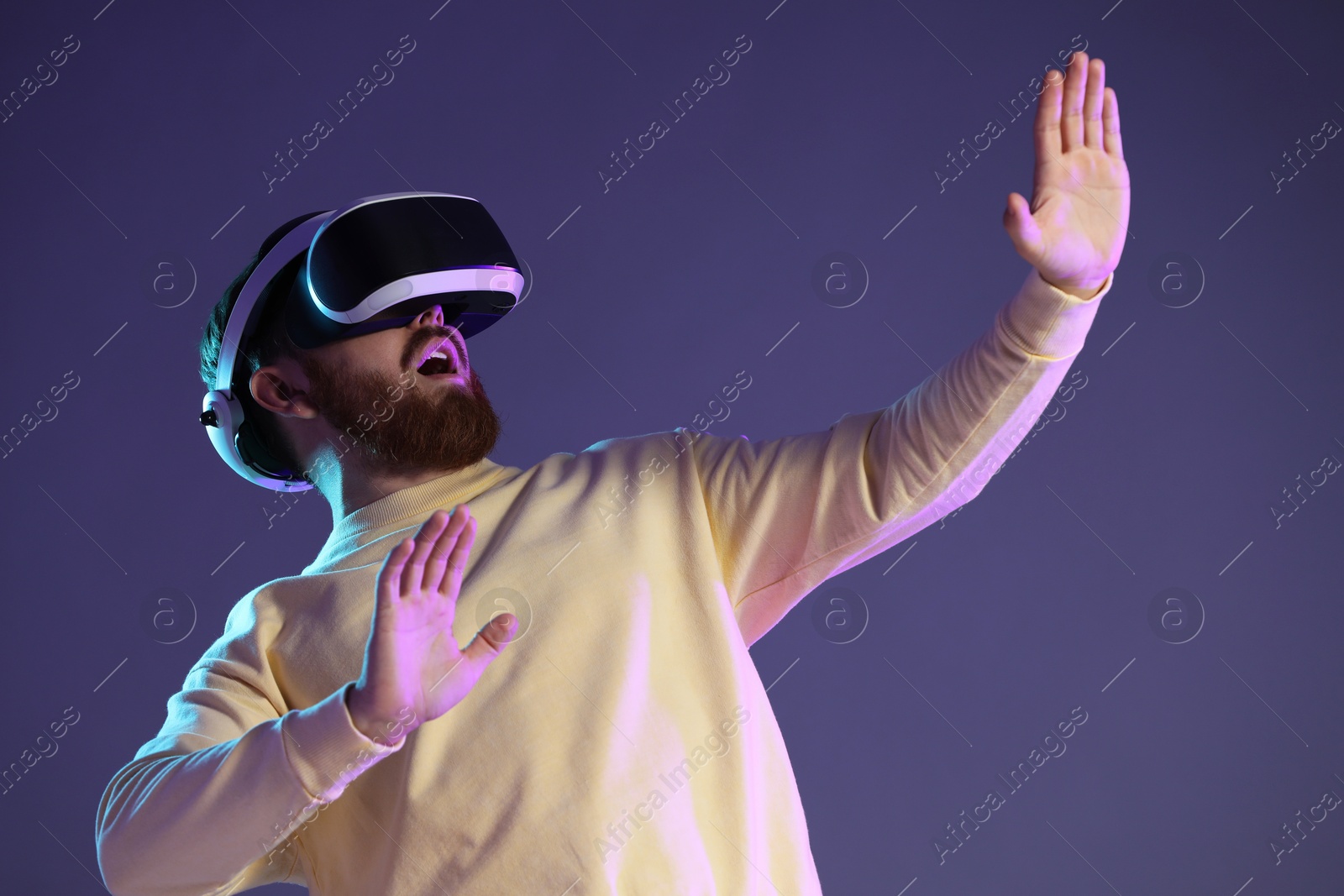 Photo of Emotional man using virtual reality headset on dark purple background