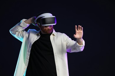 Photo of Man using virtual reality headset on dark background in neon lights. Space for text