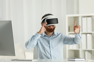 Photo of Smiling man using virtual reality headset at workplace in office