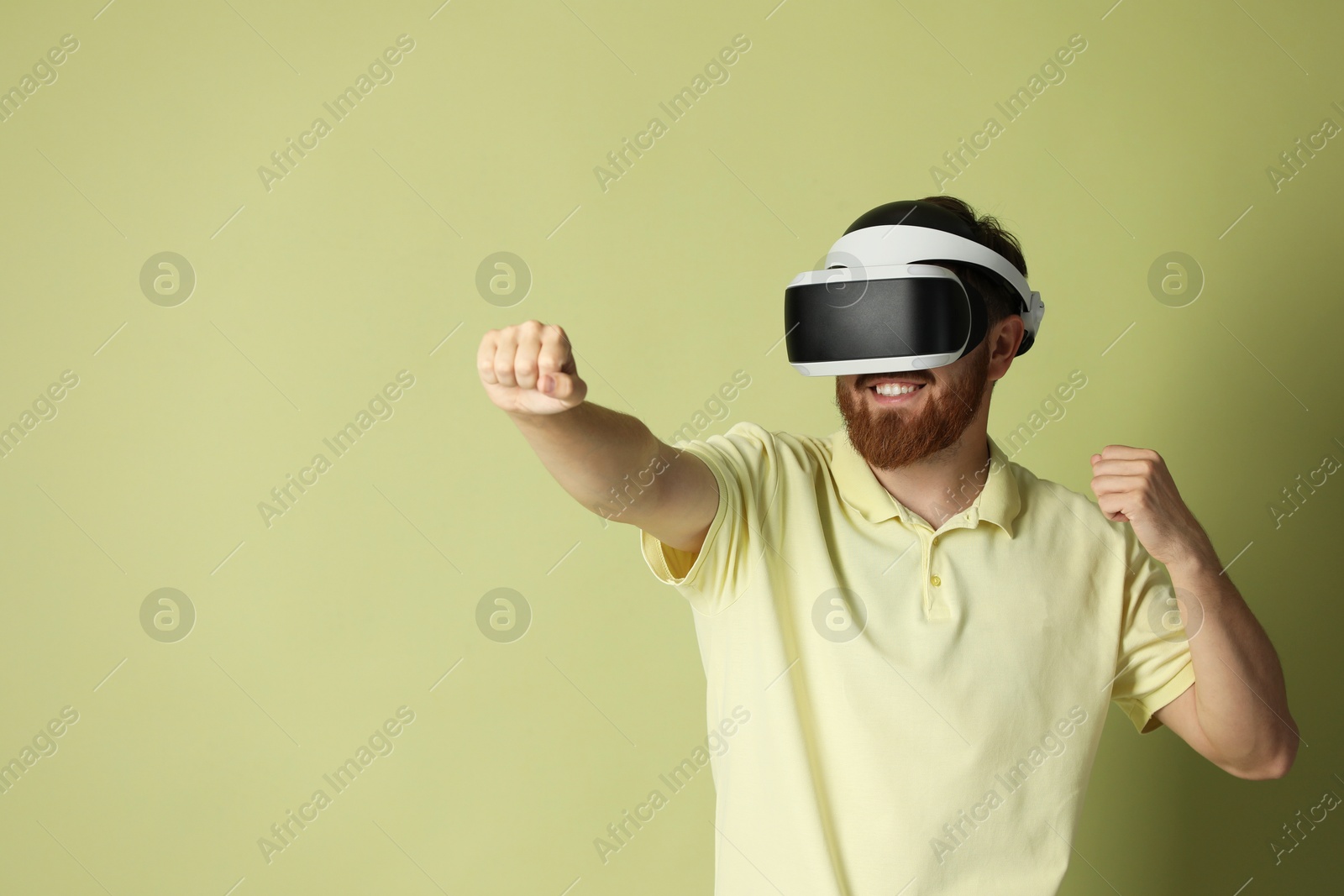 Photo of Smiling man using virtual reality headset on pale green background. Space for text