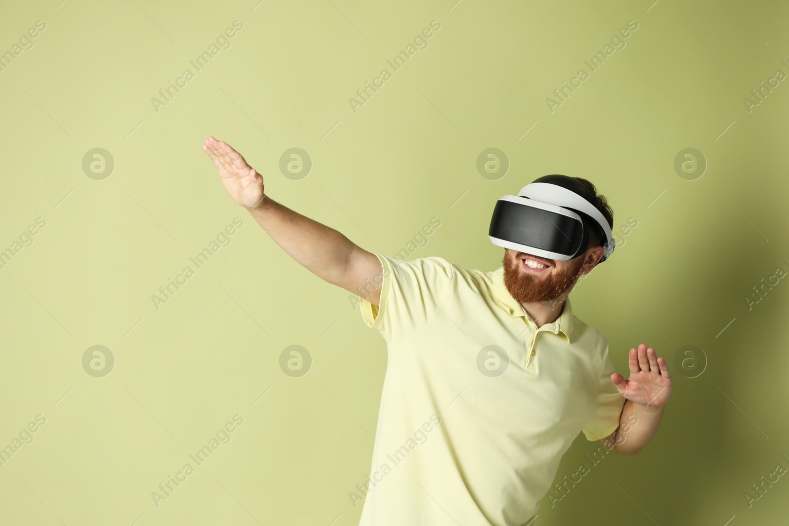 Photo of Smiling man using virtual reality headset on pale green background. Space for text