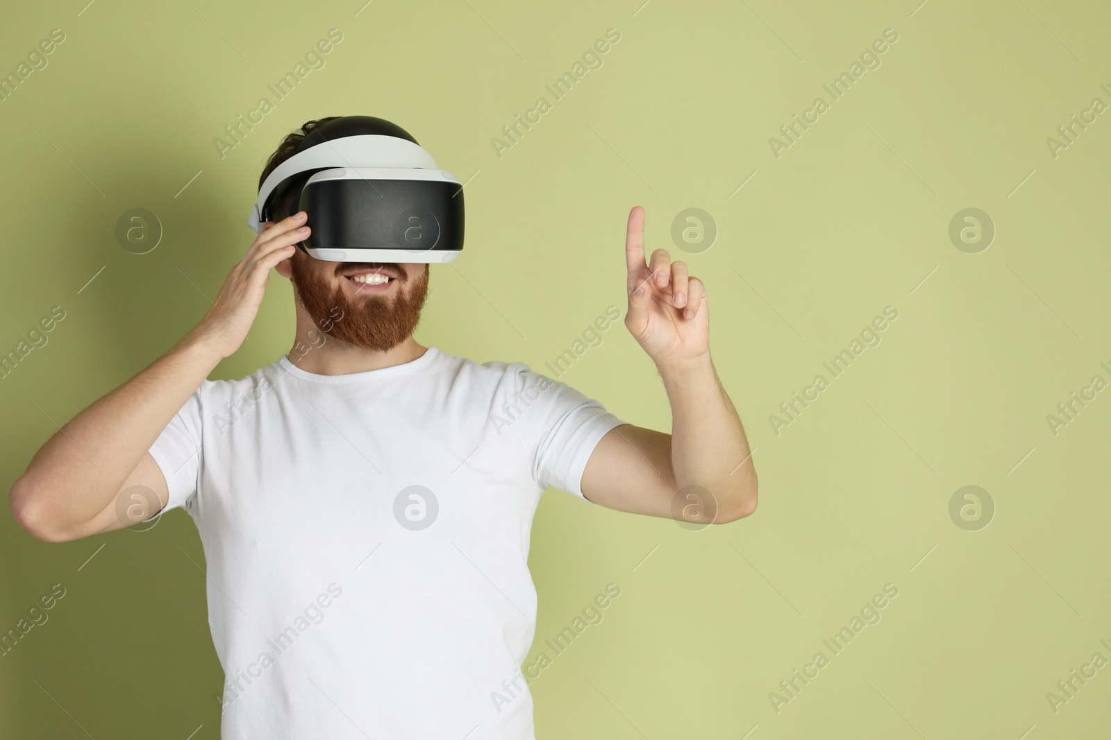 Photo of Smiling man using virtual reality headset on pale green background. Space for text