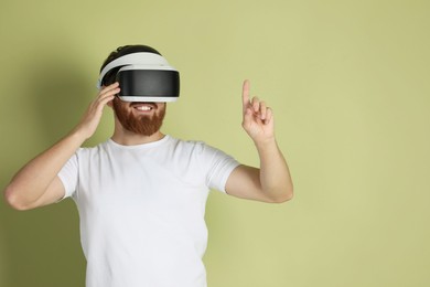 Photo of Smiling man using virtual reality headset on pale green background. Space for text
